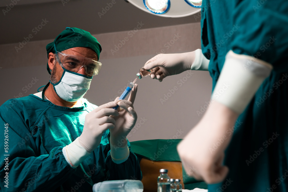 外科医生在无菌手术室用辅助器具从医用小瓶中填充注射器进行手术
