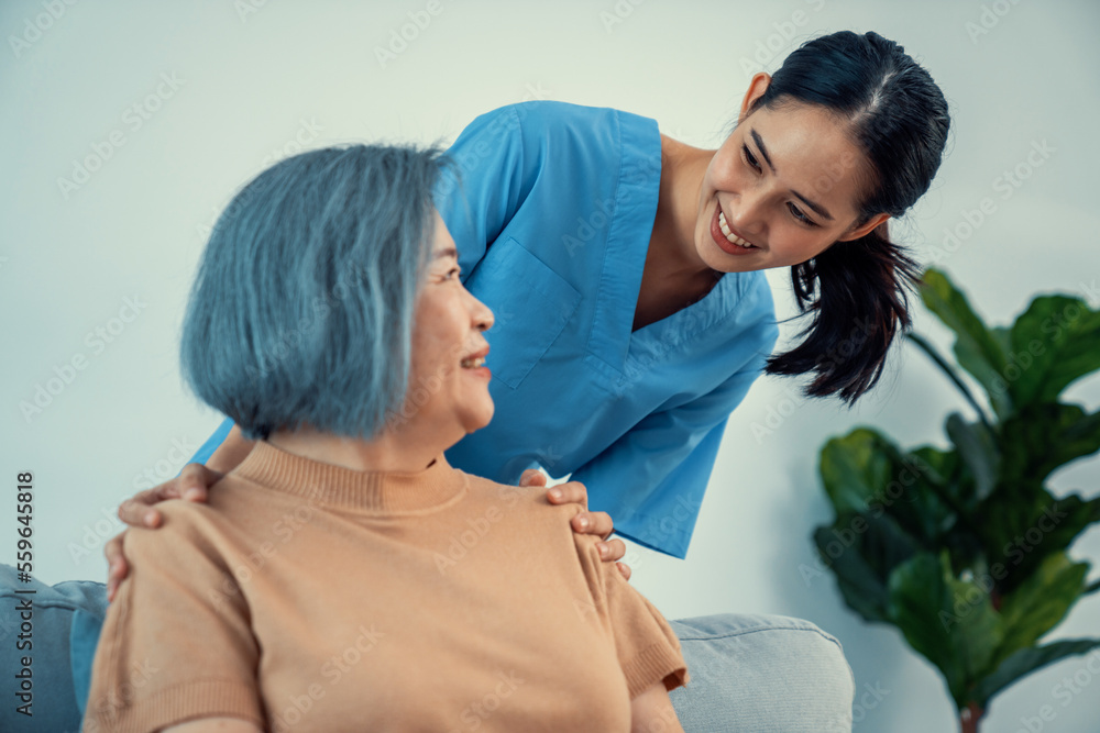 A caregiver rest her hands on the shoulders of a contented senior patient while she sitting on the s