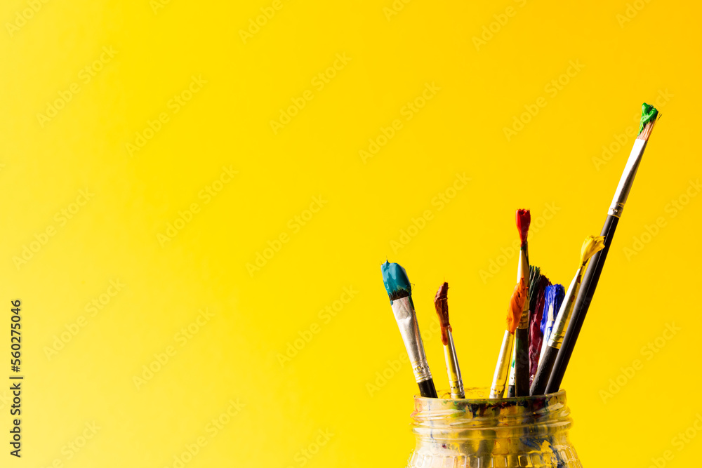 Image of close up of jar with paint brushes and copy space on yellow background