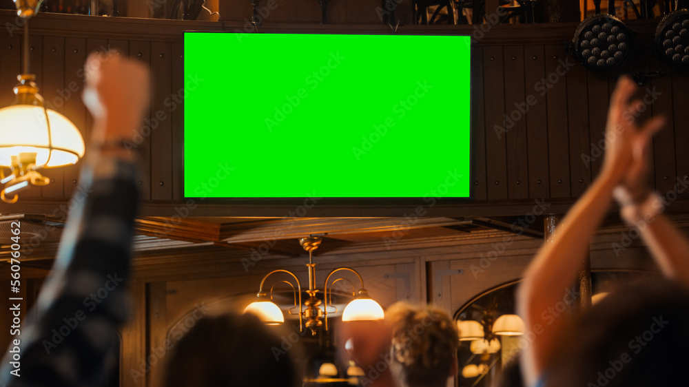 一群多元文化的朋友在酒吧里用绿屏观看电视直播的体育比赛