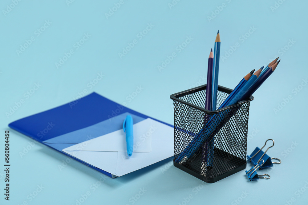 Holder with stationery, notebook and envelope on blue background