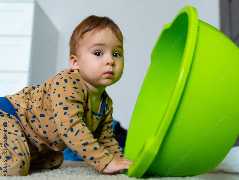 Baby playing with a bowl at home. Baby toys, toys for developing creativity. Basin for laundry