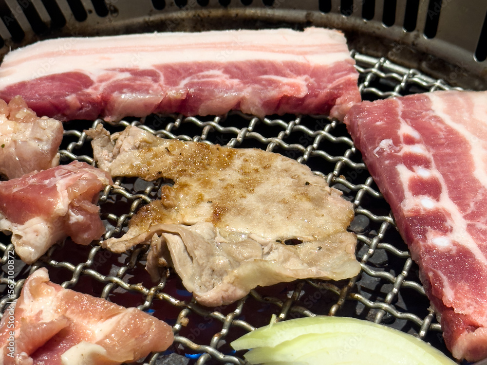 Grilling pork belly meat on a round BBQ net in restaurant for eating.