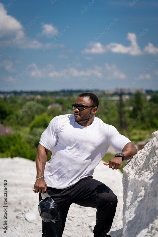 Handsome athletic man in white shirt standing outdoor. Strong big man in sunglasses outdoor.