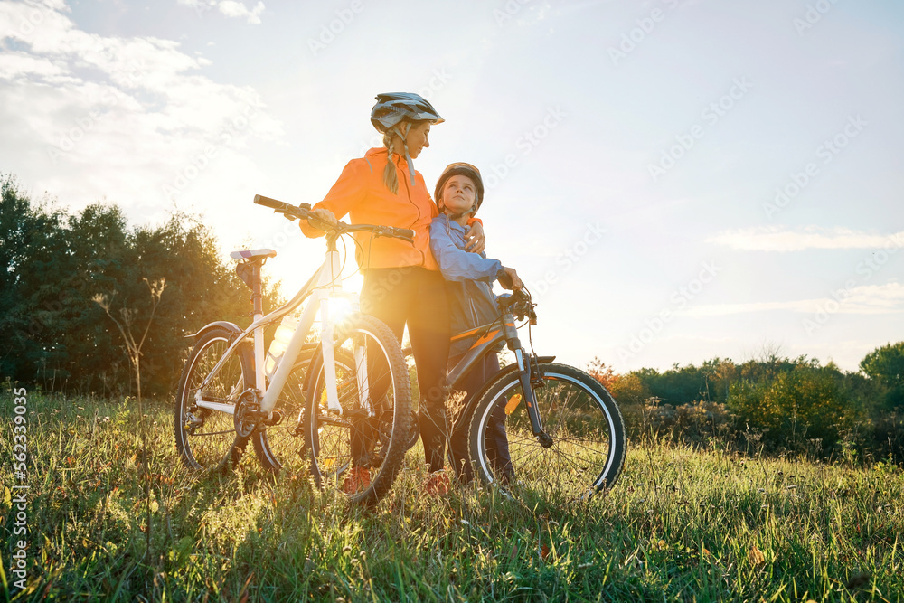 母子俩骑自行车。戴着头盔的可爱男孩在公园里的绿色草地上学习骑自行车