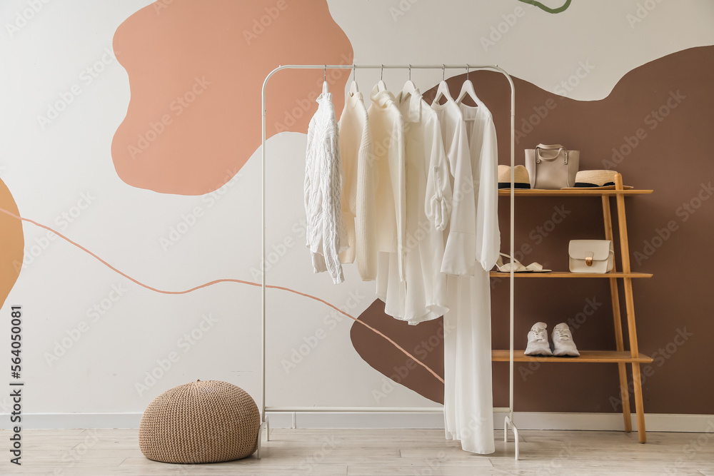 Rack with white clothes, shelving unit and accessories near color wall