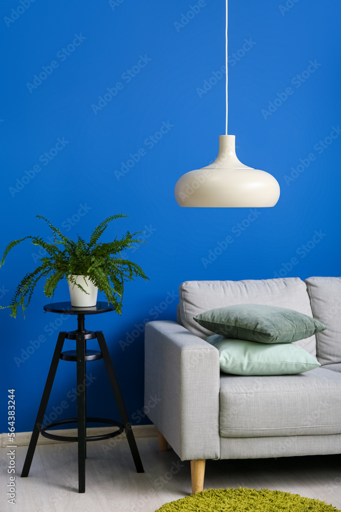 灰色沙发，蓝色墙壁附近的凳子上有垫子和室内植物