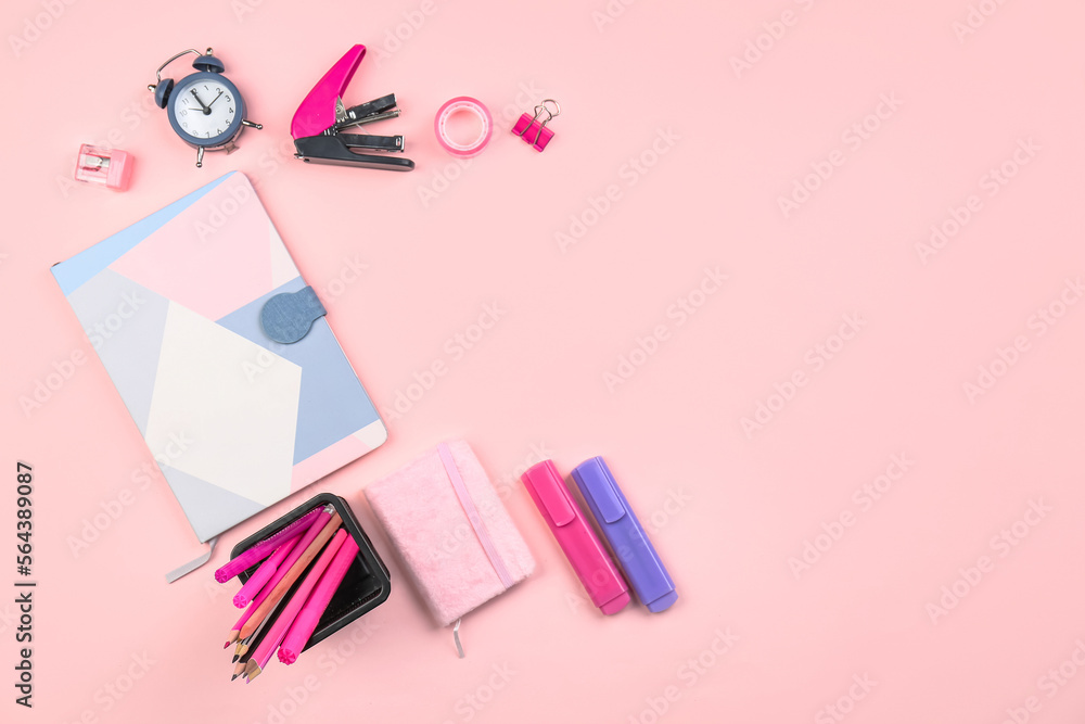 粉红色背景上有文具、笔记本和闹钟的支架