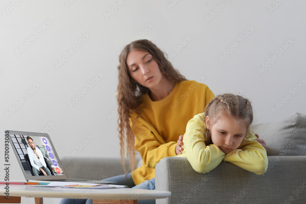 Upset little girl and her mother video chatting with psychologist on laptop at home