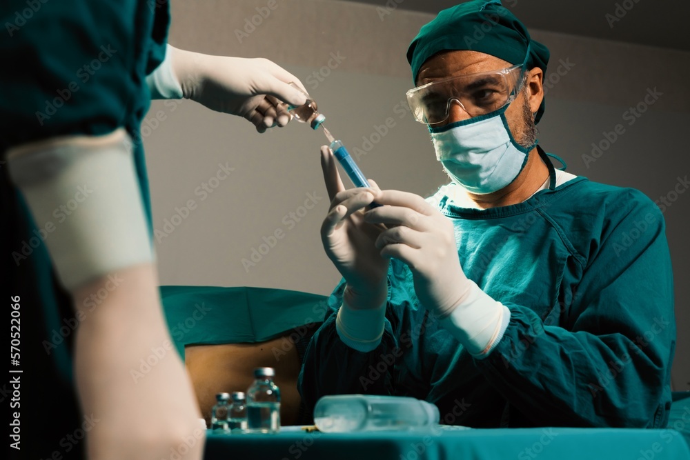Surgeon fill syringe from medical vial for surgical procedure at sterile operation room with assista