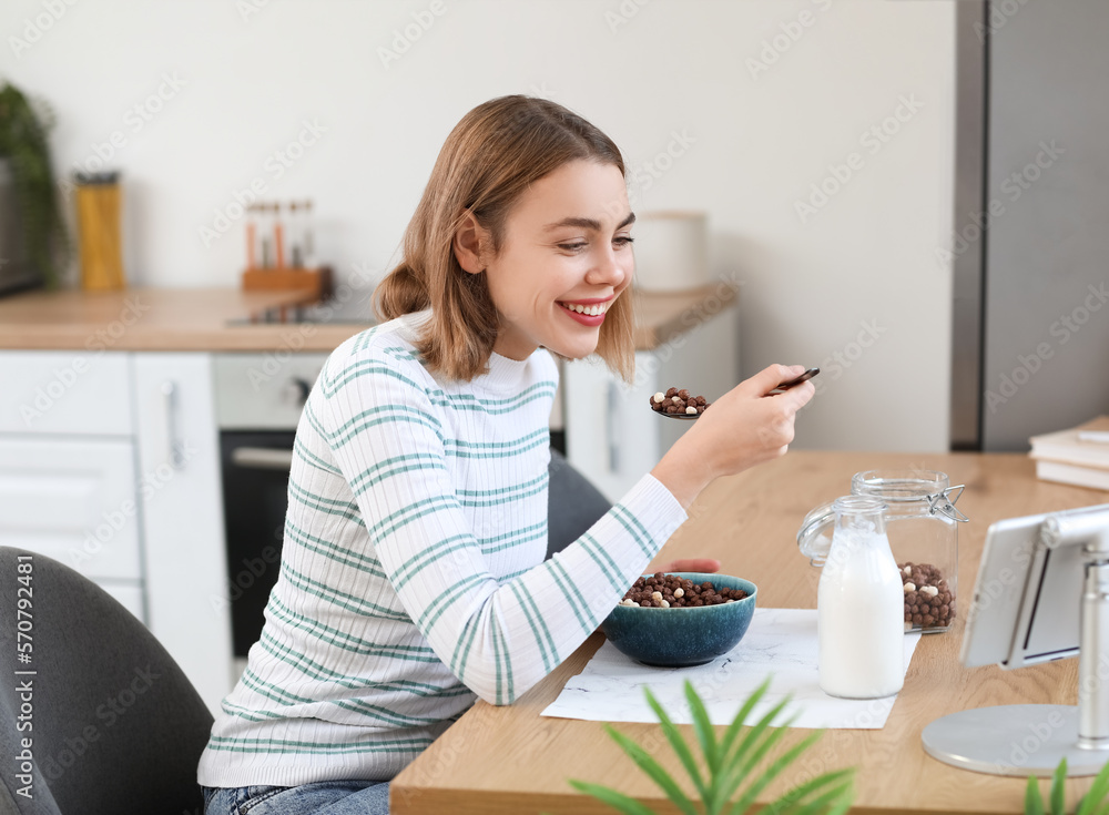 Young woman eating corn balls with spoon at table in kitchen