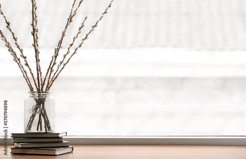 Vase with willow branches and books on windowsill in room