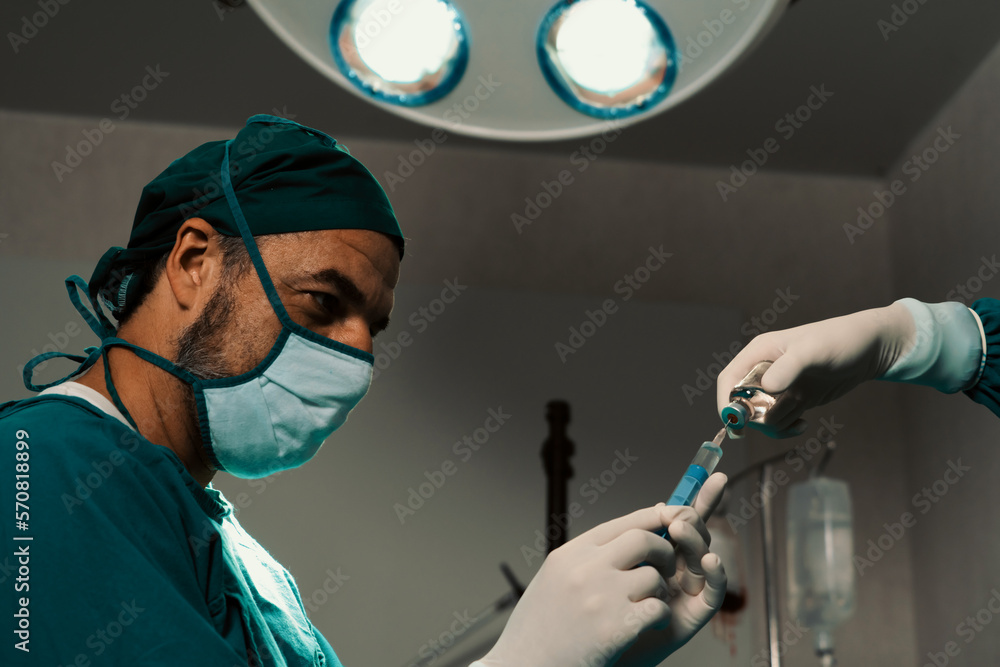 Surgeon fill syringe from medical vial for surgical procedure at sterile operation room with assista