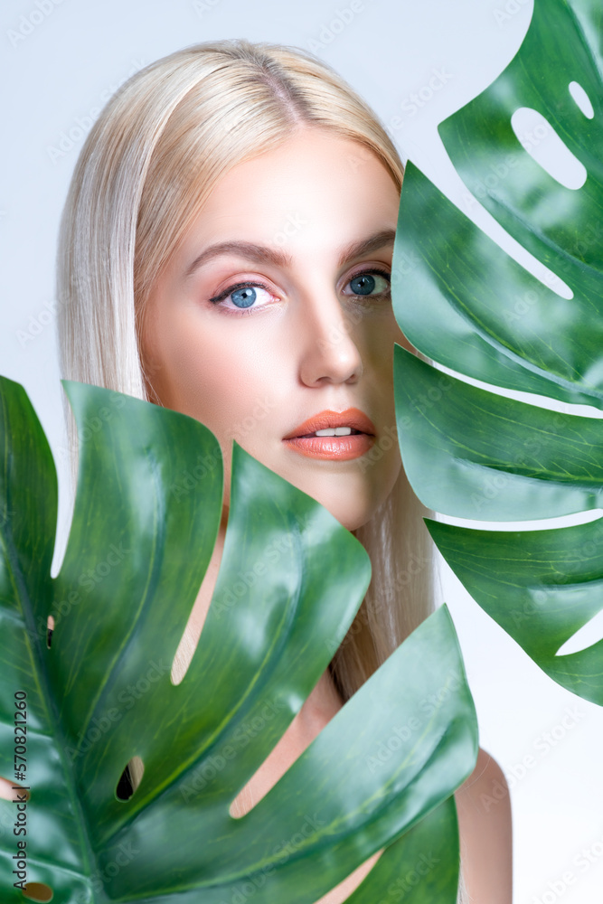 Closeup facial portrait personable woman with perfect smooth makeup holding green monstera leaves an