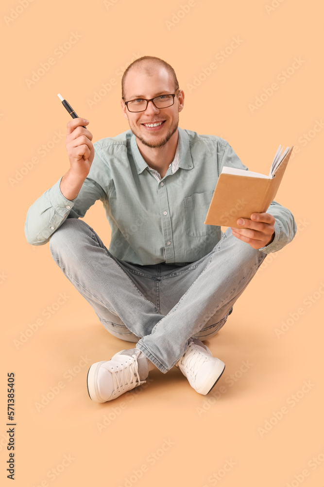 Young man in eyeglasses with disposable electronic cigarette reading book on beige background