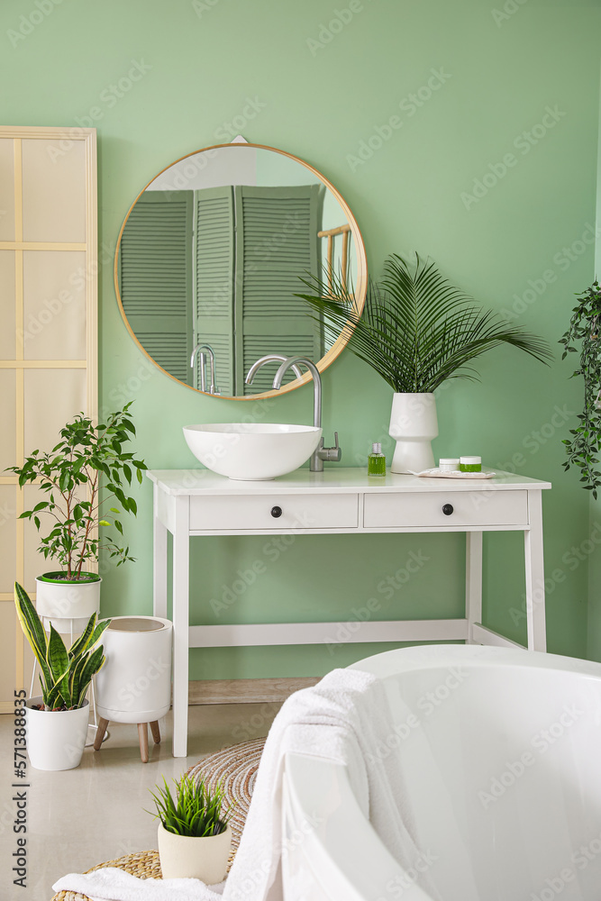 Interior of bathroom with houseplants, bathtub and ceramic sink near mirror