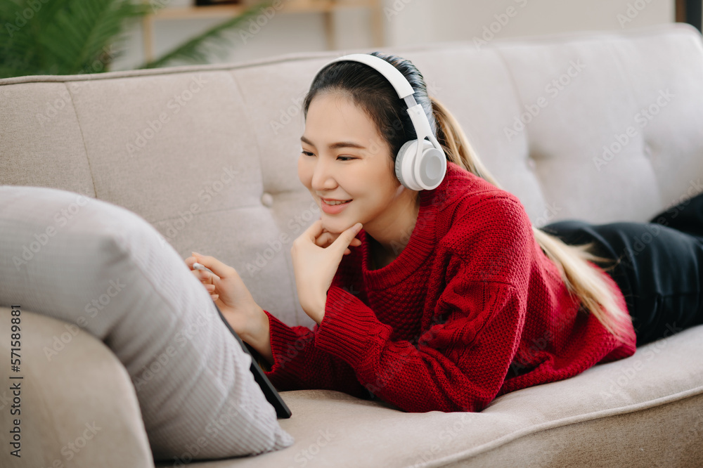 ￼Smiling girl relaxing at home, she is playing music using smartphone tablet, laptop, and wearing wh