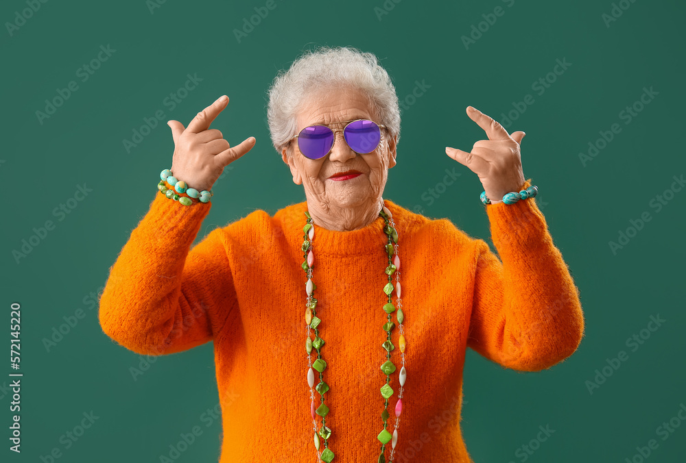 Senior woman with bright accessories showing  i love you  gesture on green background