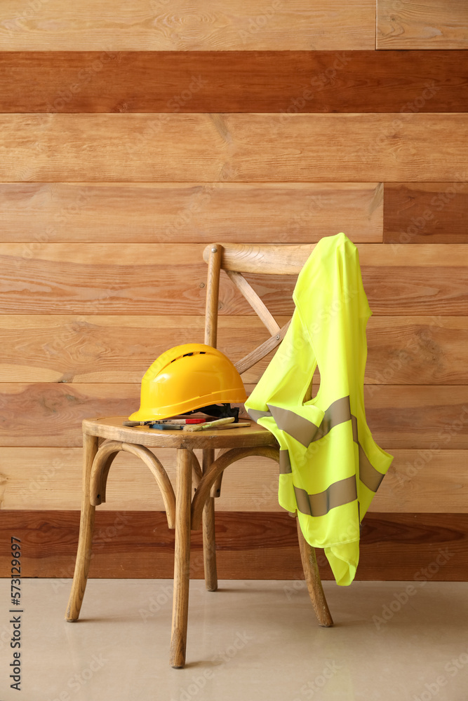 Chair with hardhat and reflective vest near wooden wall