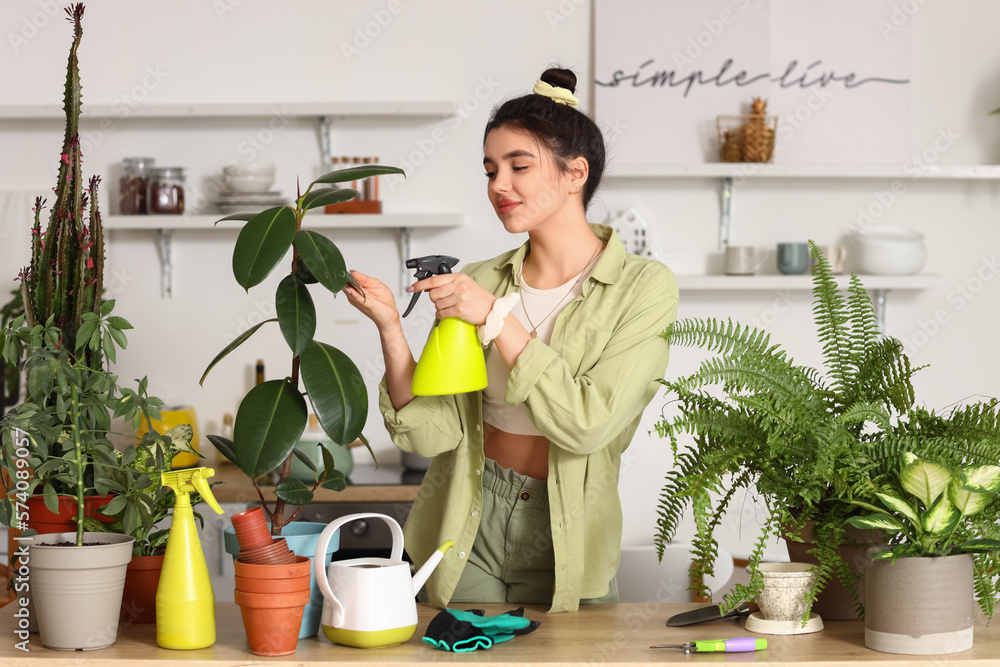 Young woman spraying green houseplants with water in kitchen