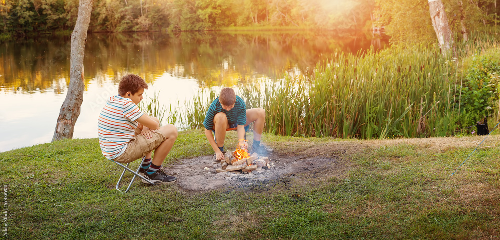 Two teenagers lighting a campfire in nature near the lake.