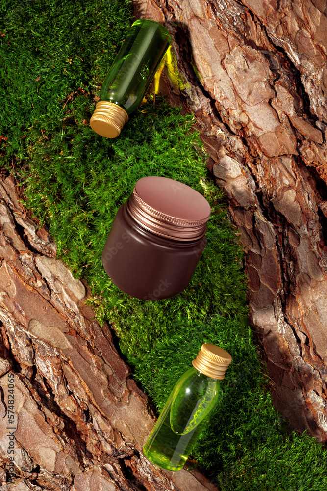 Two green glass cosmetic bottles and product mockup in brown and gold colors on textured tree bark a