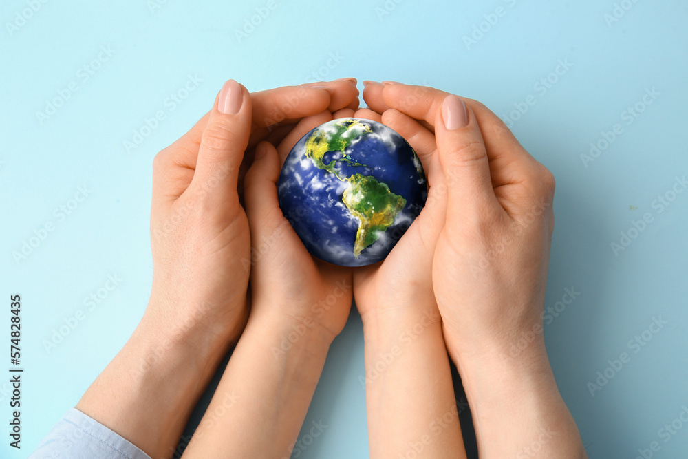 Hands of mother and child holding small planet Earth on light blue background