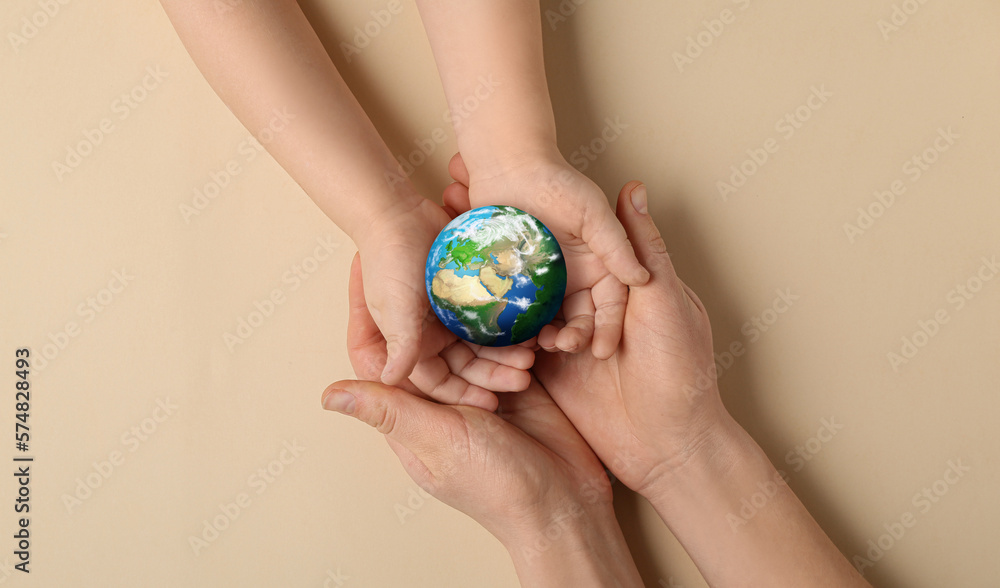 Hands of mother and child holding small planet Earth on beige background