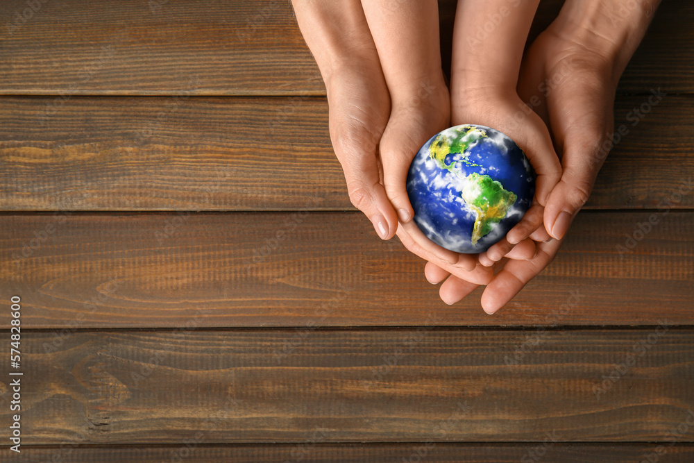 Hands of mother and child holding small planet Earth on wooden background