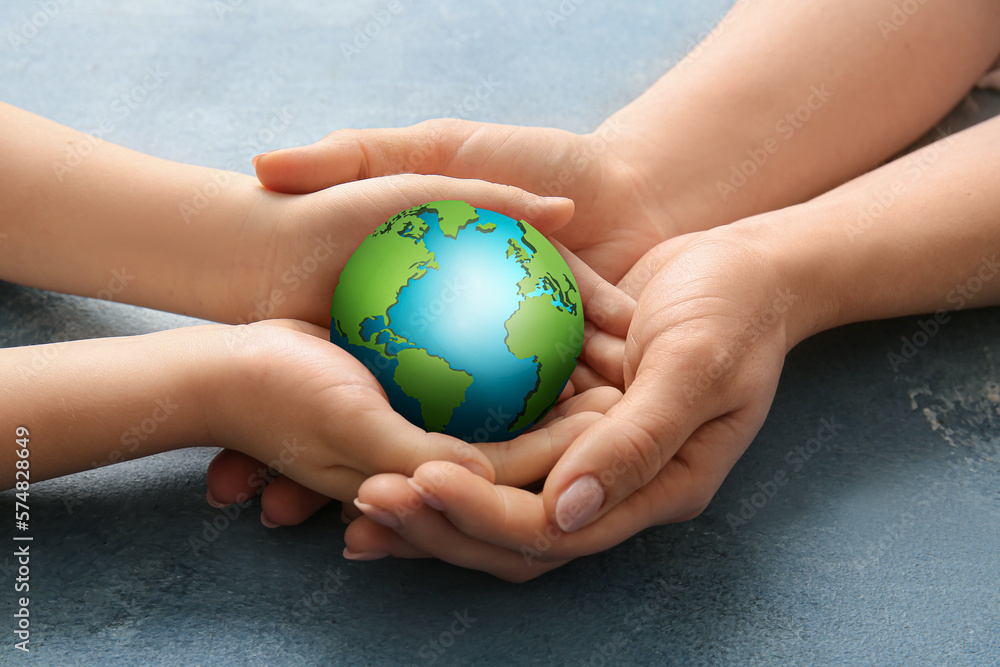Hands of mother and child holding small planet Earth on color background