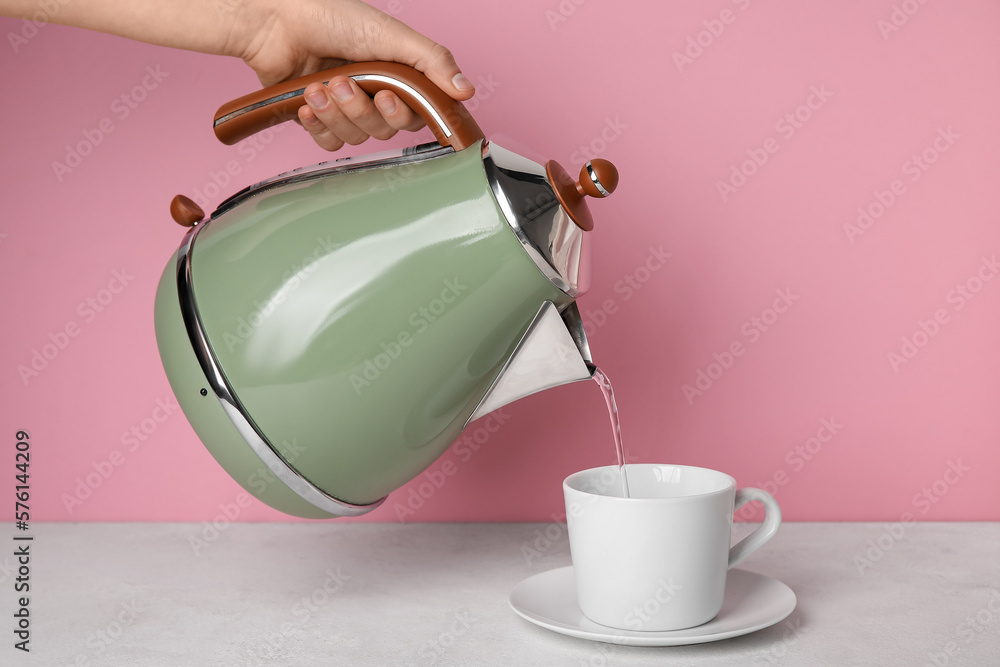 Woman pouring boiled water from kettle into cup near pink wall
