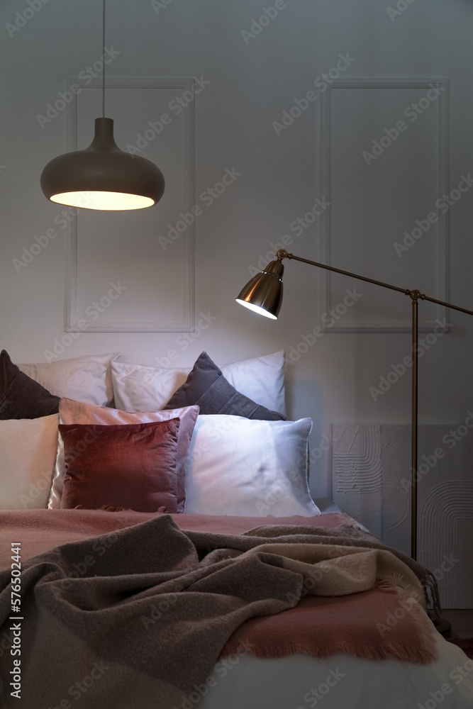 Interior of bedroom with blankets on bed and glowing lamps at night
