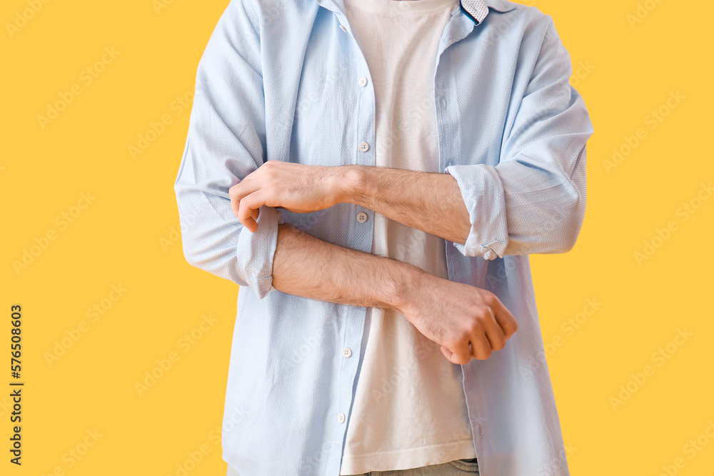 Young man rolling up his sleeve on yellow background
