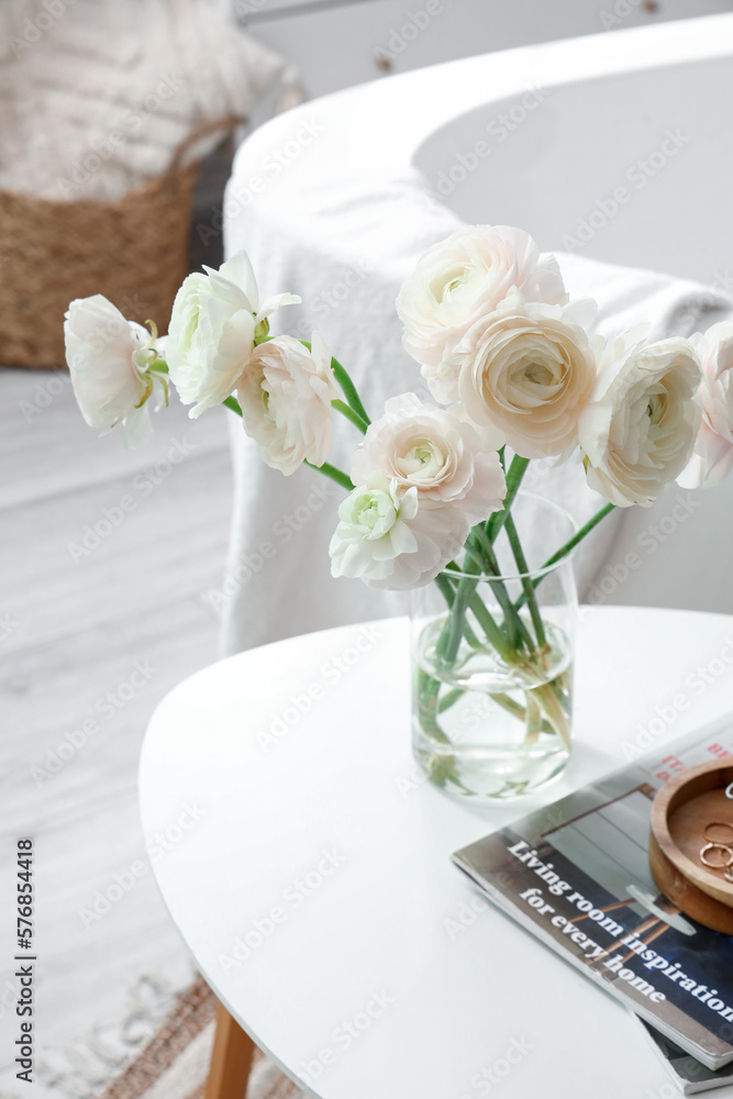 Vase with ranunculus flowers and magazines on table in bathroom, closeup
