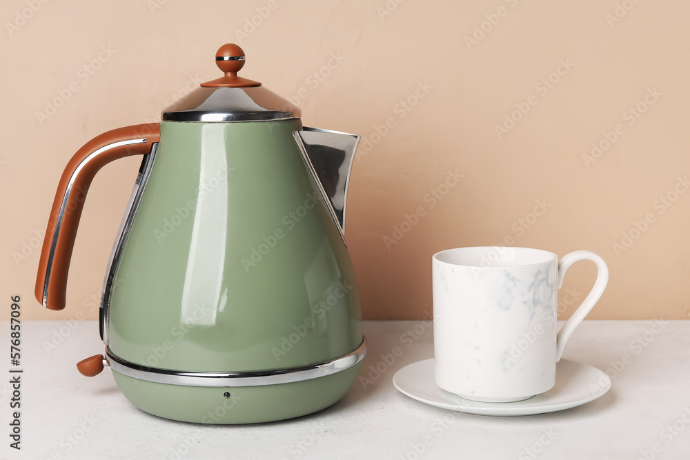 Electric kettle and cup on table near brown wall