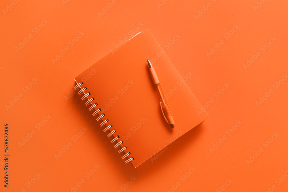 Notebook with pen on orange background