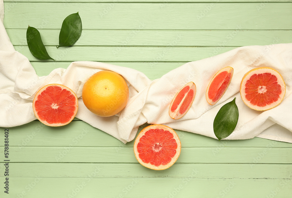 Composition with ripe grapefruits, napkin and plant leaves on color wooden background