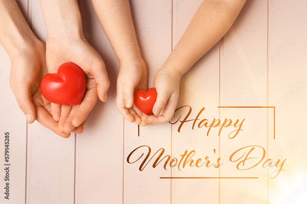 Hands of woman and child with red hearts on wooden background. Greeting card for Mothers Day