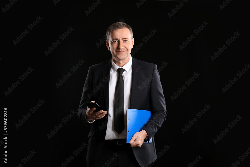Mature business consultant with mobile phone and clipboard on dark background