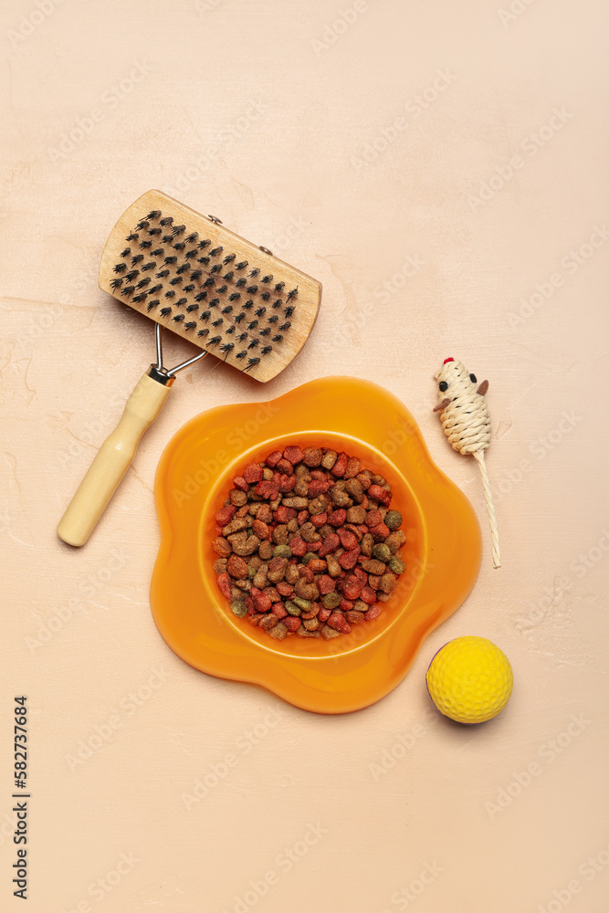 Bowl of dry pet food, grooming brush and toys on color background