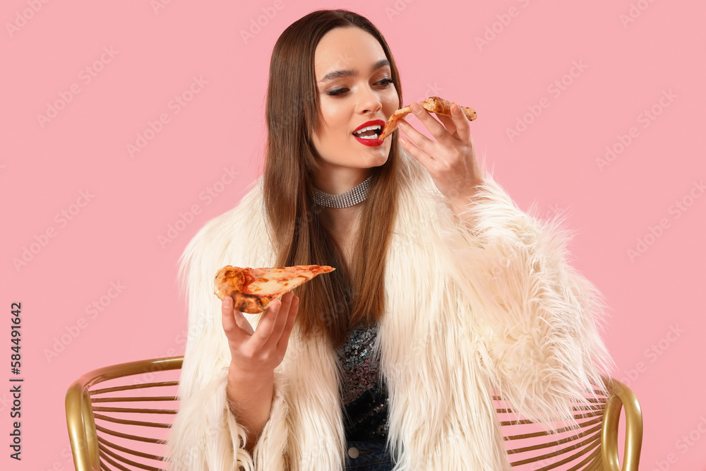 Stylish young woman with tasty pizza sitting in armchair on pink background