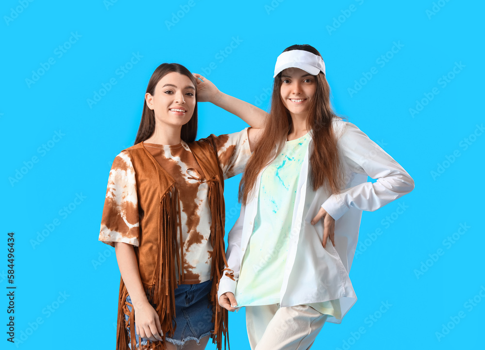 Stylish young women in tie-dye t-shirts on light blue background