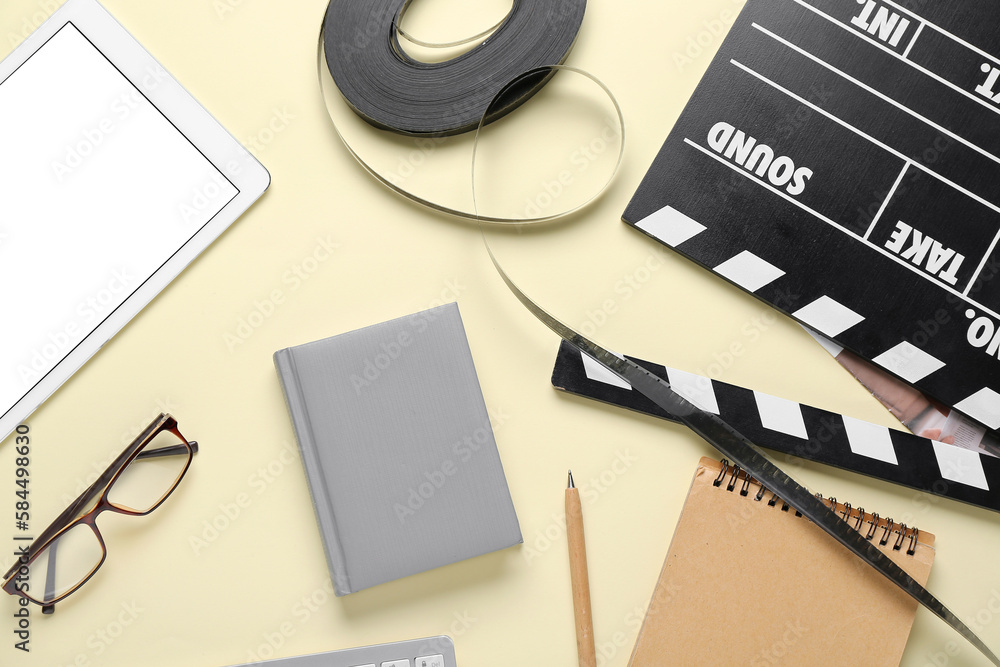 Notebooks with movie clapper, film reel and tablet computer on beige background