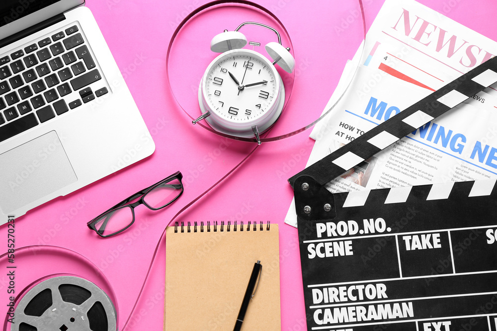 Movie clapper with alarm clock, newspapers, film reel and laptop on pink background