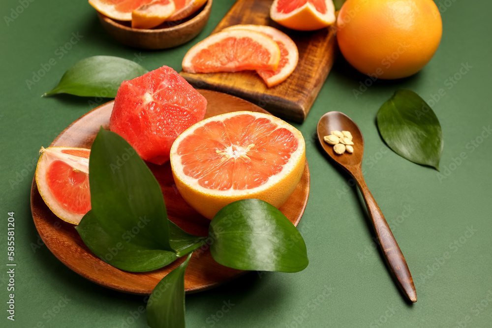Plate with ripe grapefruits and plant leaves on green background, closeup