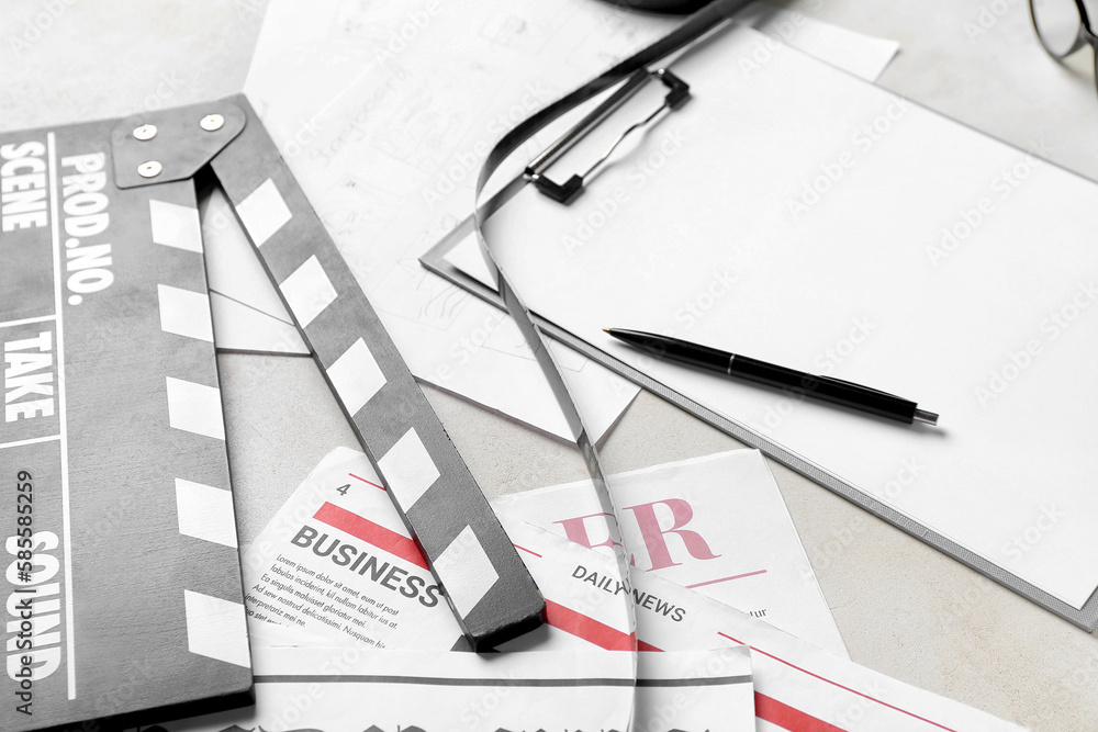 Clipboard with film, newspapers and movie clapper on light background