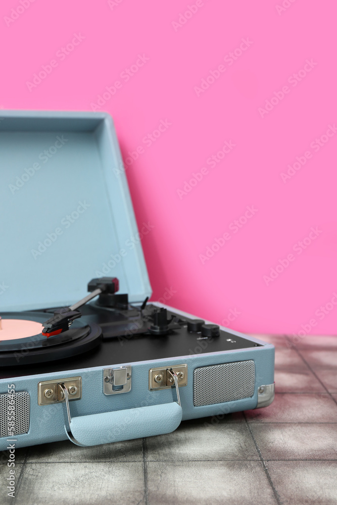 Record player with vinyl disk on table near pink wall