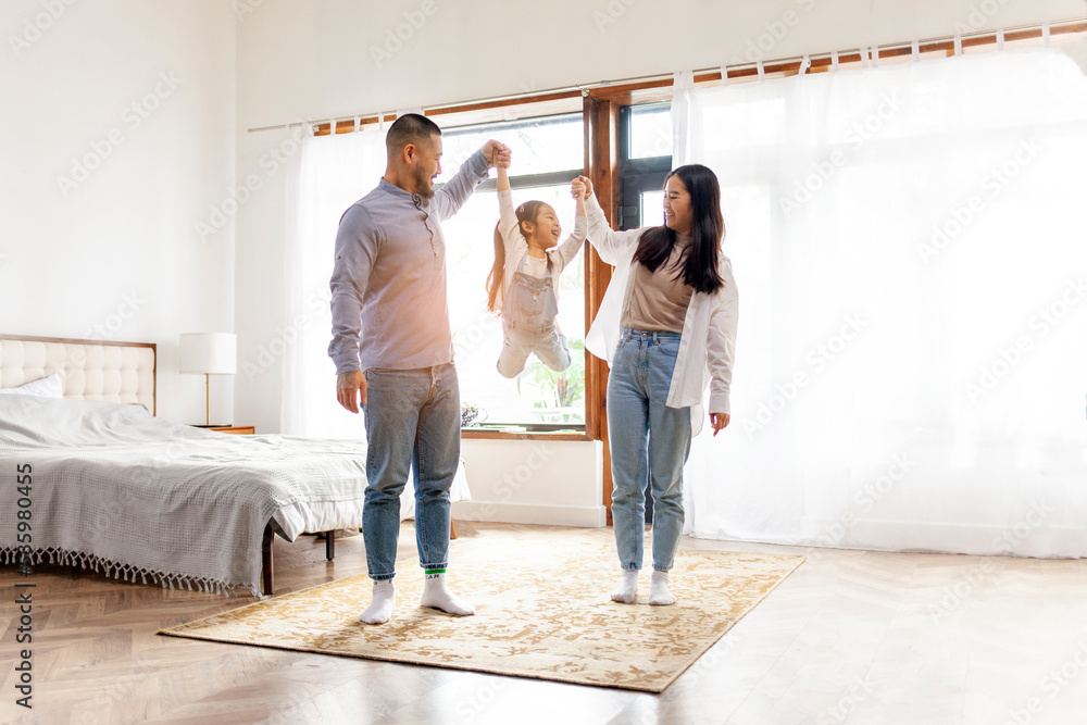 happy Asian family with little daughter stands at home in the bedroom and rejoices, dad and mom rais