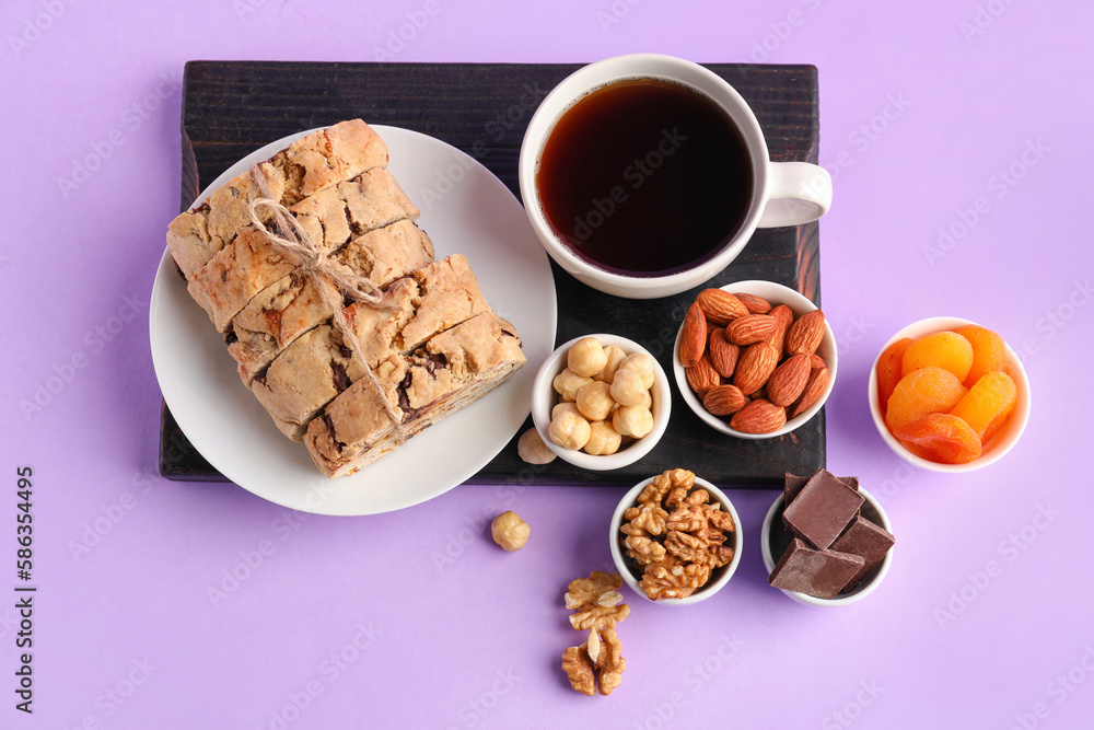 Board with biscotti cookies, chocolate, nuts, dried apricots and cup of coffee on lilac background