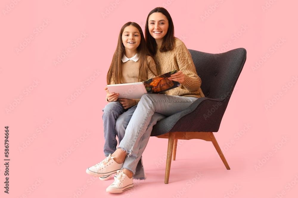 Little girl and her mother with book sitting in armchair on pink background